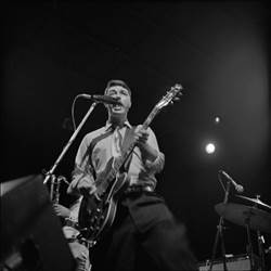 A person playing guitar and singing into a microphone

Description automatically generated